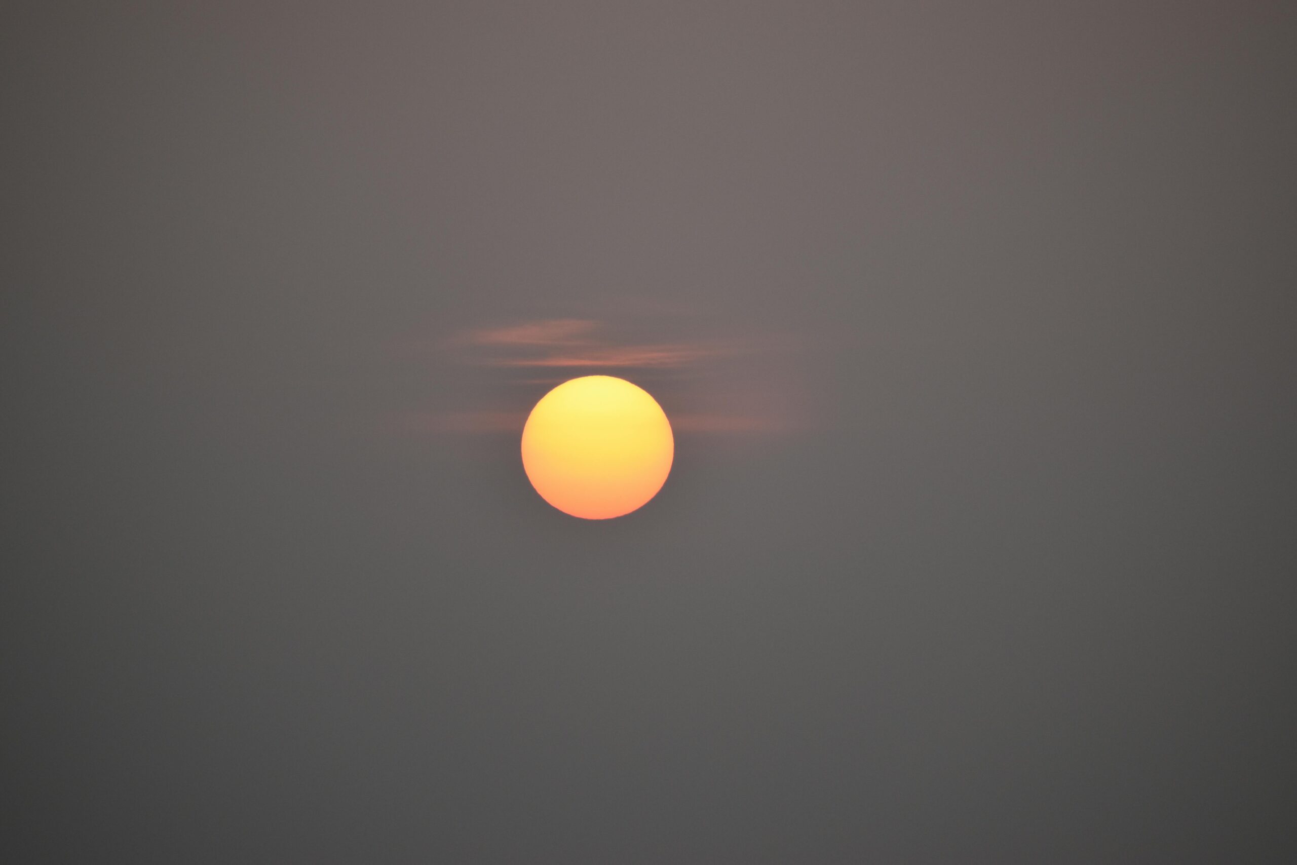 Tranquil image of the sun setting behind light clouds with a gray sky in India.